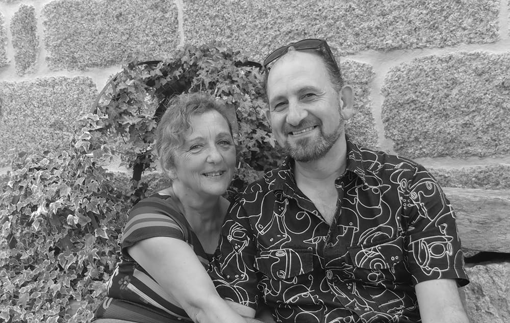 Fidel y Violeta, los anfitriones, sentados sonriendo contra el muro de piedra cubierto de hiedra.